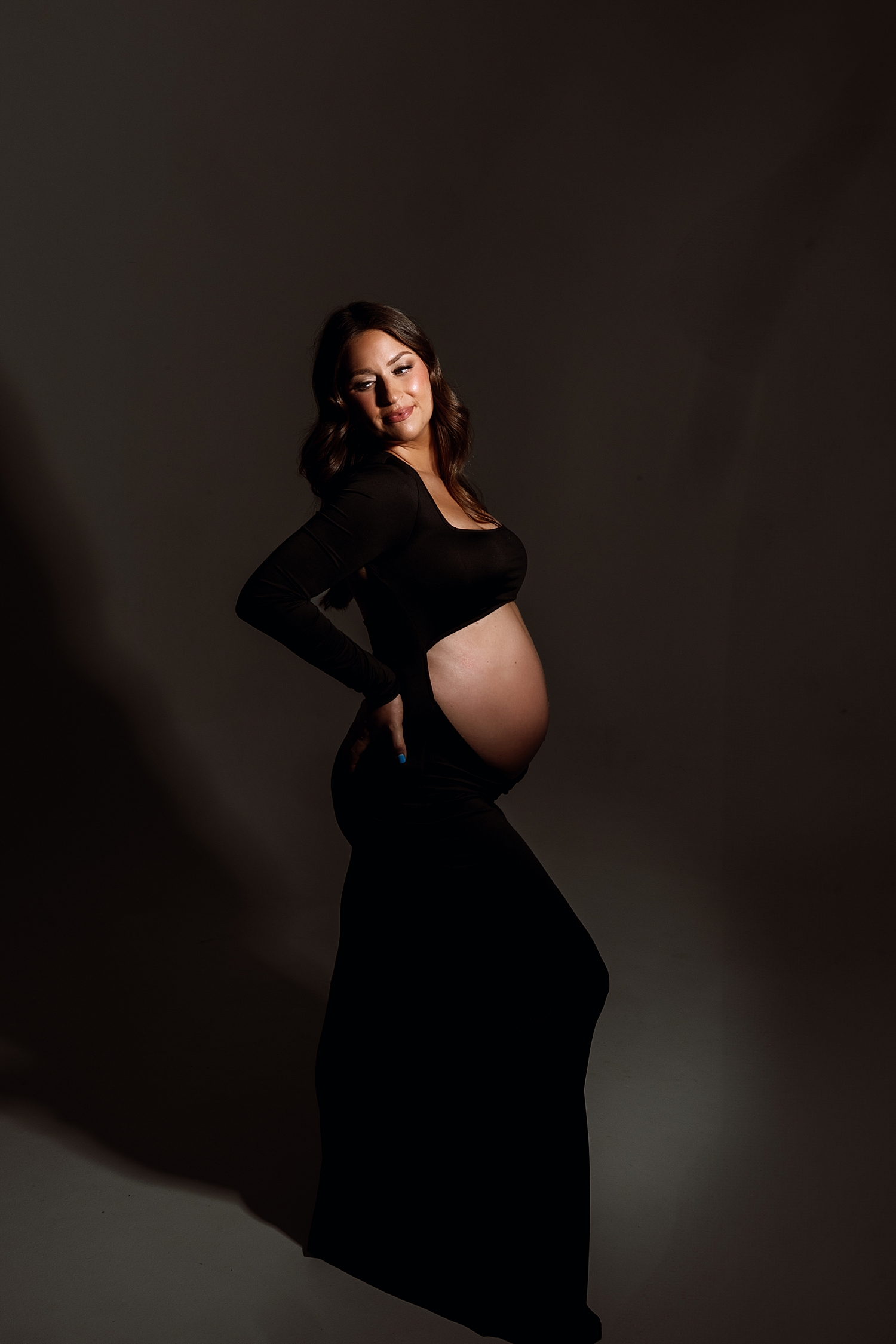 model with pregnant bump in black stands in studio glamour lighting