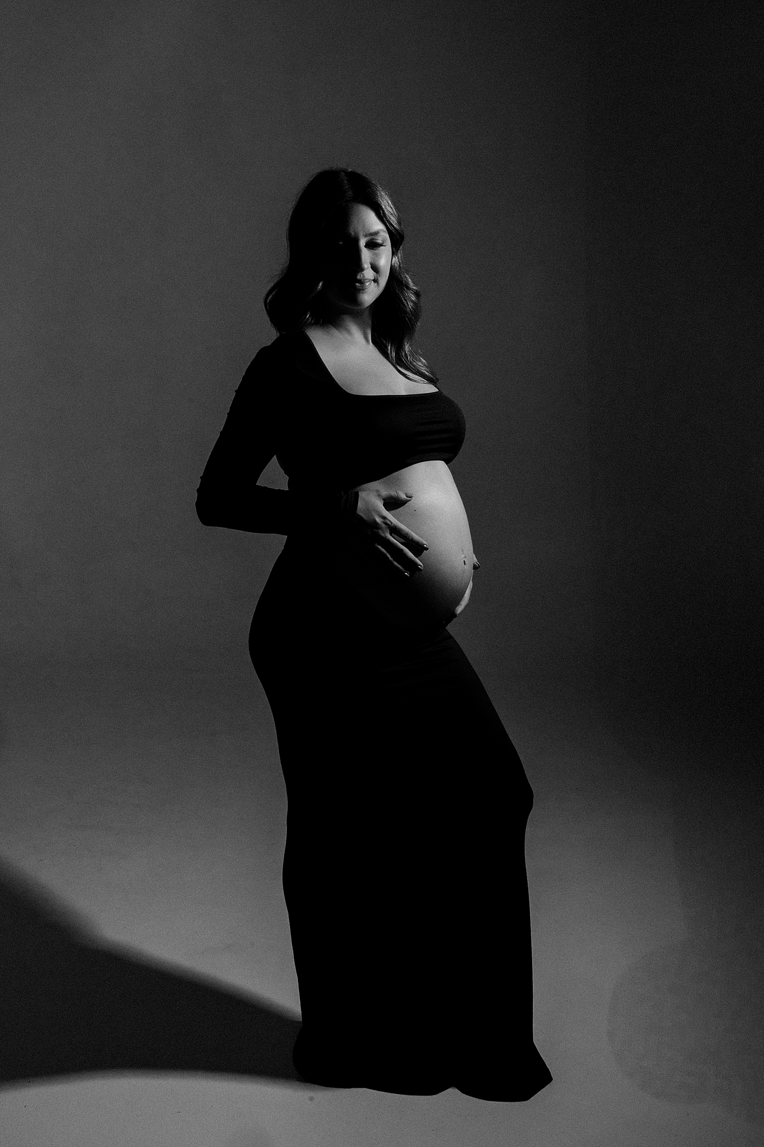 woman holds her pregnant belly in studio glamour lighting