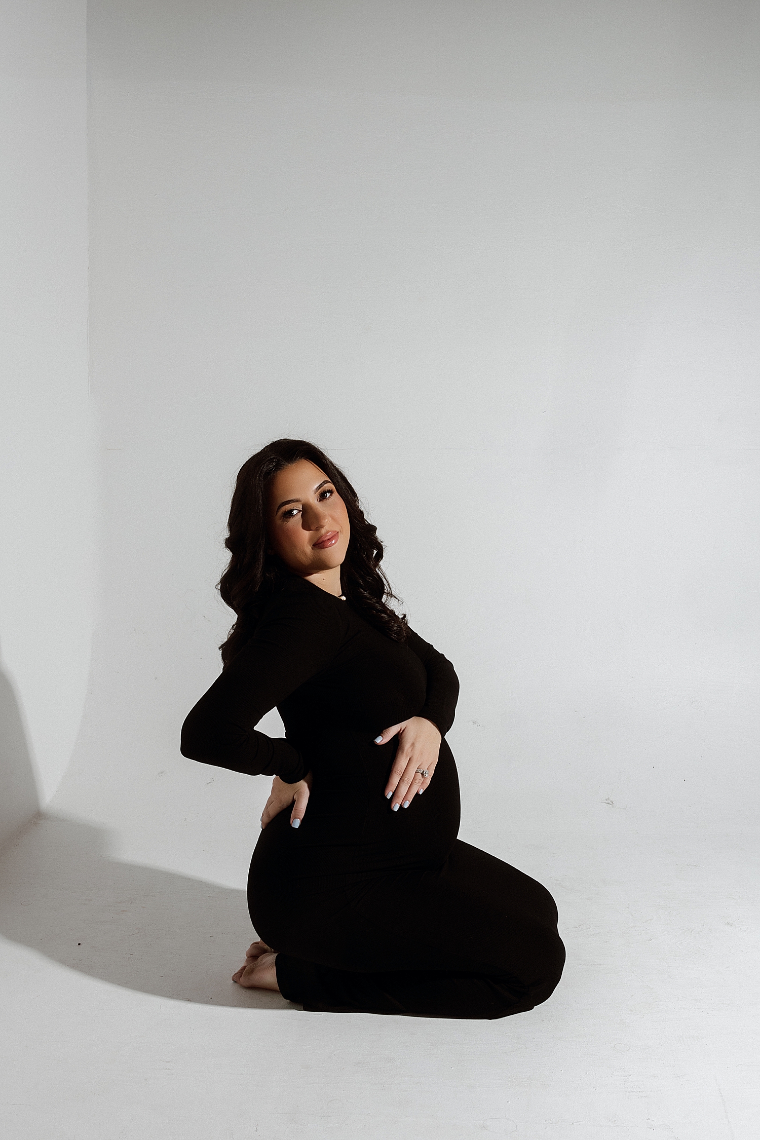 woman kneels on white studio floor for Studio Glam Mama Session